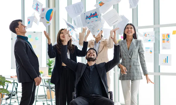 Millennial Asian Indian male female businessman businesswoman group in multinational multicultural company throwing paperwork documents in air celebrating job achievement deal done together in office.