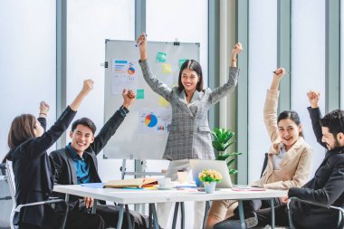 Asian businesswoman presenter in formal suit standing smiling holding pen pointing at graph chart document on whiteboard presenting information to multinational male female colleagues in meeting room
