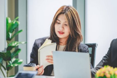Closeup shot of two young millennial Asian professional cheerful female businesswomen in formal suit sitting holding tablet computer busy working with colleague in company conference meeting room.