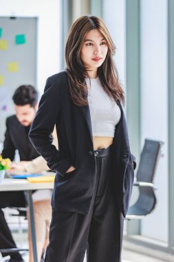 Portrait shot of millennial Asian cheerful successful professional businesswoman entrepreneur in formal suit standing smiling crossed arms in meeting room while employee and colleague brainstorming.