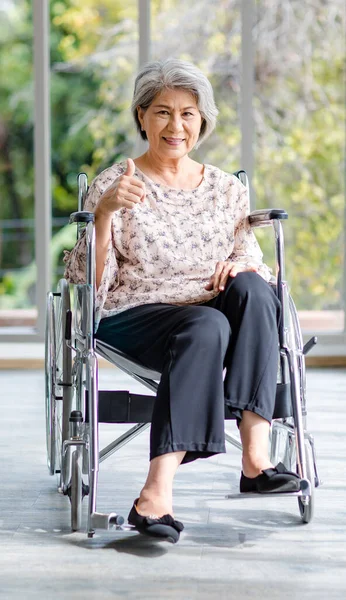 Asian happy cheerful old senior healthy gray hair retired pensioner disability handicapped grandmother sitting smiling on wheelchair using touchscreen smartphone surfing browsing social media online.