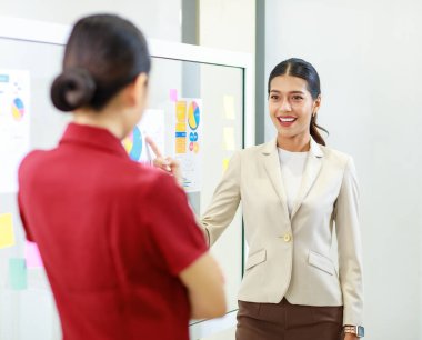 Asyalı genç, güzel, profesyonel, başarılı iş kadını gülümseyip grafik çizelgesini sunuyor. Veri belgelerini cam tahtada kadın ve erkek meslektaşlarına sunuyor..