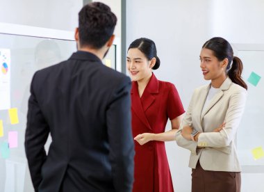 Asyalı genç, güzel, profesyonel, başarılı iş kadını gülümseyip grafik çizelgesini sunuyor. Veri belgelerini cam tahtada kadın ve erkek meslektaşlarına sunuyor..
