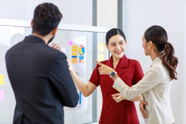 Asyalı genç, güzel, profesyonel, başarılı iş kadını gülümseyip grafik çizelgesini sunuyor. Veri belgelerini cam tahtada kadın ve erkek meslektaşlarına sunuyor..