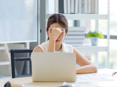 Asian stressed exhausted tired female businesswoman secretary working late and hard sitting at workplace in company take off glasses hold hand massaging painful shoulder from office syndrome symptom.