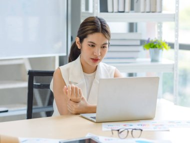 Asian stressed exhausted tired female businesswoman secretary working late and hard sitting at workplace in company take off glasses hold hand massaging painful shoulder from office syndrome symptom.