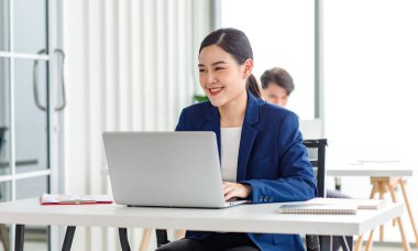 Closeup shot of millennial Asian young beautiful smart professional female businesswoman employee in formal suit sitting working on workstation desk typing laptop notebook computer in company office.