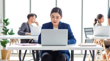 Closeup shot of millennial Asian young beautiful smart professional female businesswoman employee in formal suit sitting working on workstation desk typing laptop notebook computer in company office.