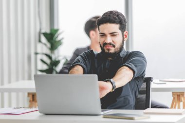 Indian stressed depressed exhausted bearded male businessman sitting at workstation with laptop computer close eyes hold hand on head feeling tired and sleepy after working late overtime last night.