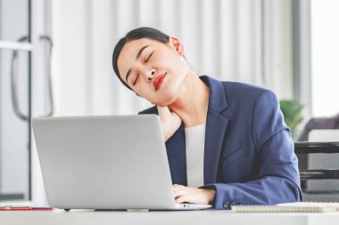 Asian stressed exhausted tired female businesswoman secretary working late and hard sitting at workplace in company take off glasses hold hand massaging painful shoulder from office syndrome symptom.