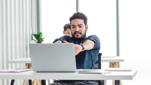 Indian stressed depressed exhausted bearded male businessman sitting at workstation with laptop computer close eyes hold hand on head feeling tired and sleepy after working late overtime last night.