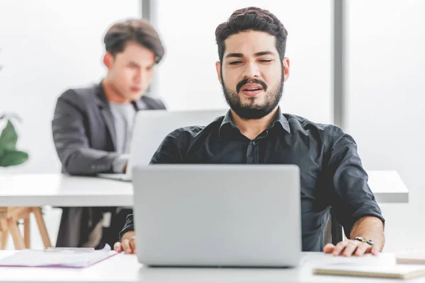 Indian stressed depressed exhausted bearded male businessman sitting at workstation with laptop computer close eyes hold hand on head feeling tired and sleepy after working late overtime last night.