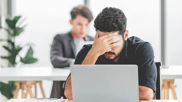 Indian stressed depressed exhausted bearded male businessman sitting at workstation with laptop computer close eyes hold hand on head feeling tired and sleepy after working late overtime last night.