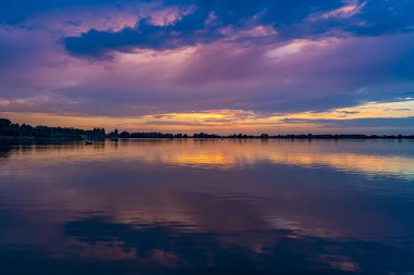 Bu neredeyse rüzgarsız akşamda son tekneler limana doğru yelken açar ve sadece batan güneş gökyüzünde güzel renkler yaratır.