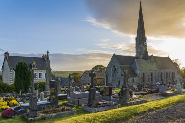 Fransa, Normandie 'de Montpinchon kilisesinin yanındaki eski mezarlıkta gün batımı.