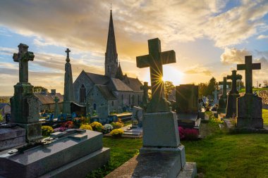 Batan güneş Fransa 'nın Normandiya kentindeki Montpinchon kilisesinin yanındaki eski mezarlıkta bir cenaze anıtının arkasında kayboluyor.
