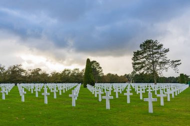 Fransa, Normandiya 'daki Colleville-sur-Mer yakınlarındaki etkileyici Amerikan askeri mezarlığında bulutlu gökyüzünün altında sonsuz beyaz haçlar var.