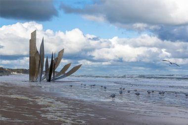 Bu savaş anıtının yanında, birçok martı etkileyici gökyüzünün olduğu bir günde Fransa 'nın Normandiya' nın Vierville-sur-mer kasabası yakınlarındaki Omaha plajında yürüyor.