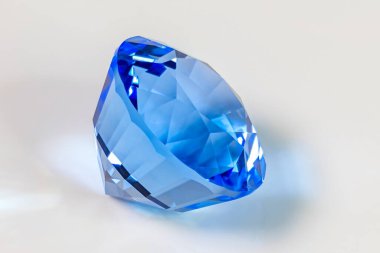 Detail photo (focus stacking) of a self-cut Synthetic Quartz with Deep Blue color and Mixed, Pavillion step cut, placed on a white acrylic glass surface with the crown facing top right