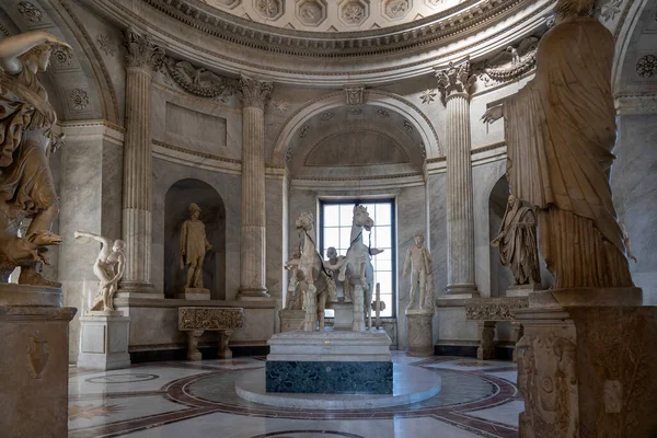 A room in one of the museums in Vatican City, Rome, with several marble statues of people and in the center a marble statue of a chariot