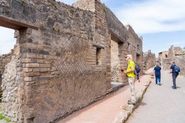 İtalya 'nın harabe şehri Pompeii' nin ana caddelerinden birinin kalıntıları arasında yürüyen turistler görülüyor.