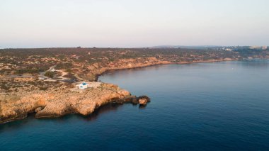 Kıbrıs Rum Kesimi 'nin Famagusta kentinin Cavo Greco Protaras kentindeki Agioi Anargyroi kilisesinde, kıyı şeridi günbatımının ve tarihi beyaz şapelin havadan görünüşü. Gündoğumunda Ammochostos di 'de turist manzaralı kayalık Ayioi Anargiroi kilisesi, mağaralar, plaj manzaralı.