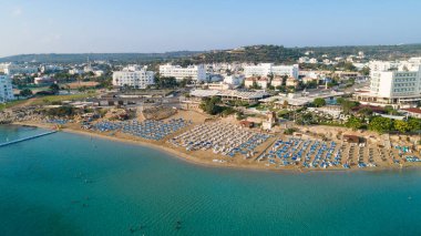 Protaras, Paralimni, Famagusta, Kıbrıs 'taki İncir ağaçlarının kuş bakışı görüntüsü. Ünlü turistik eğlence ailesi, tekneleri, güneşlikleri, restoranları, su sporları olan kumlu plajlar yaz tatillerinde denizde yüzen insanlar..