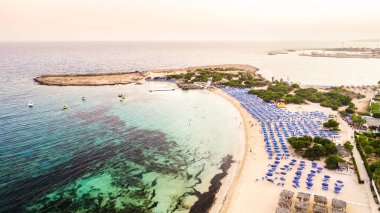 Ünlü Makronissos sahil şeridi Ayia Napa, Famagusta, Kıbrıs 'ın havadan kuş bakışı manzarası. Günbatımında Agia Napa 'da altın kum, güneşlik, deniz restoranları ve yaz tatilleri ile turistik mekan Makronisos Körfezi..