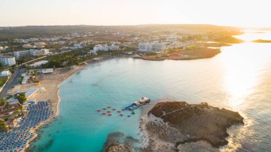 Ünlü Nissi sahil şeridi Ayia Napa, Famagusta, Kıbrıs 'ın havadan kuş bakışı manzarası. Gündoğumunda, Agia Napa 'da yaz tatillerinde altın kum, güneşlik yataklar ve deniz restoranlarıyla birlikte turistik bölge körfezi..