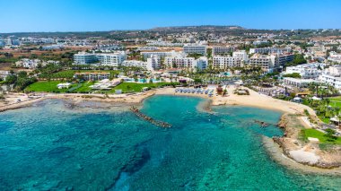 Protaras, Paralimni, Famagusta, Kıbrıs 'taki Pernera plajının kuş bakışı görüntüsü. Güneş yatakları, su sporları, oteller, restoranlar, yaz tatillerinde denizde yüzen insanlar....
