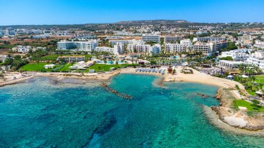 Aerial bird's eye view of Pernera beach in Protaras, Paralimni, Famagusta, Cyprus. The famous tourist attraction golden sandy bay with sunbeds, water sports, hotels, restaurants, people swimming in sea on summer holidays from above. clipart