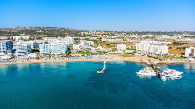 Protaras, Paralimni, Famagusta, Kıbrıs 'taki Fig Tree' deki Sunrise plajının havadan kuş bakışı görüntüsü. Altın kumu, tekneleri, güneşliği, restoranları, su sporları, yaz tatillerinde denizde yüzen insanları olan ünlü turistik aile körfezi.