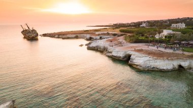Günbatımında Kıbrıs Rum Kesimi 'nin Pegeia kentindeki terk edilmiş gemi enkazı EDRO' ya kuşların bakış açısı. Pafos 'taki Coral Bay yakınlarındaki deniz mağaralarında Peyia kayalıklarında karaya oturmuş paslı gemi enkazı kıyıda duruyor..