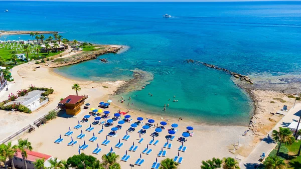 Aerial bird\'s eye view of Pernera beach in Protaras, Paralimni, Famagusta, Cyprus. The famous tourist attraction golden sandy bay with sunbeds, water sports, hotels, restaurants, people swimming in sea on summer holidays from above.