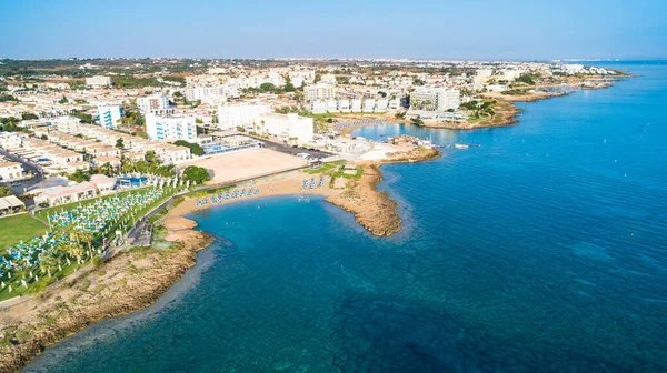 Aerial bird\'s eye view of Pernera beach in Protaras, Paralimni, Famagusta, Cyprus. The famous tourist attraction golden sandy bay with sunbeds, water sports, hotels, restaurants, people swimming in sea on summer holidays from above.