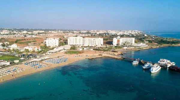 Aerial bird's eye view of Sunrise beach at Fig tree in Protaras, Paralimni, Famagusta, Cyprus. The famous tourist attraction family bay with golden sand, boats, sunbeds, restaurants, water sports, people swimming in sea on summer holidays, from above