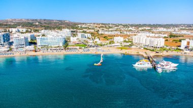 Protaras, Paralimni, Famagusta, Kıbrıs 'taki Fig Tree' deki Sunrise plajının havadan kuş bakışı görüntüsü. Altın kumu, tekneleri, güneşliği, restoranları, su sporları, yaz tatillerinde denizde yüzen insanları olan ünlü turistik aile körfezi.