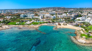 Protaras, Paralimni, Famagusta, Kıbrıs 'taki Pernera plajının kuş bakışı görüntüsü. Güneş yatakları, su sporları, oteller, restoranlar, yaz tatillerinde denizde yüzen insanlar....