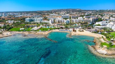 Aerial bird's eye view of Pernera beach in Protaras, Paralimni, Famagusta, Cyprus. The famous tourist attraction golden sandy bay with sunbeds, water sports, hotels, restaurants, people swimming in sea on summer holidays from above. clipart