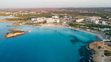 Ünlü Nissi sahil şeridi Ayia Napa, Famagusta, Kıbrıs 'ın havadan kuş bakışı manzarası. Gündoğumunda, Agia Napa 'da yaz tatillerinde altın kum, güneşlik yataklar ve deniz restoranlarıyla birlikte turistik bölge körfezi..