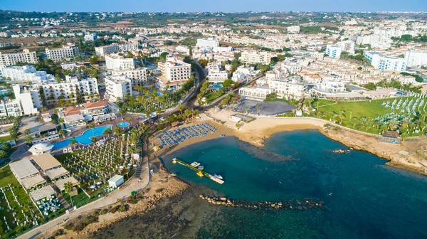 Aerial bird's eye view of Pernera beach in Protaras, Paralimni, Famagusta, Cyprus. The famous tourist attraction golden sandy bay with sunbeds, water sports, hotels, restaurants, people swimming in sea on summer holidays from above.