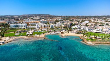 Protaras, Paralimni, Famagusta, Kıbrıs 'taki Pernera plajının kuş bakışı görüntüsü. Güneş yatakları, su sporları, oteller, restoranlar, yaz tatillerinde denizde yüzen insanlar....