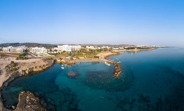 Aerial bird\'s eye view of Green bay in Protaras, Paralimni, Famagusta, Cyprus. The famous tourist attraction diving location rocky beach with boats, sunbeds, restaurants, water sports, people swimming in sea on summer holidays, from above.