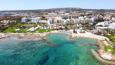 Aerial bird's eye footage view of Pernera beach in Protaras, Paralimni, Famagusta, Cyprus. The famous tourist attraction golden sandy bay with sunbeds, sun umbrellas people swimming in sea from above