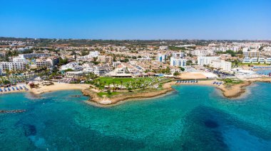 Protaras, Paralimni, Famagusta, Kıbrıs 'taki Pernera plajının kuş bakışı görüntüsü. Güneş yatakları, su sporları, oteller, restoranlar, yaz tatillerinde denizde yüzen insanlar....
