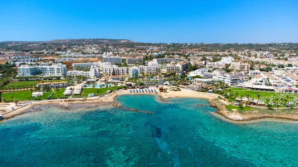 Aerial bird\'s eye view of Pernera beach in Protaras, Paralimni, Famagusta, Cyprus. The famous tourist attraction golden sandy bay with sunbeds, water sports, hotels, restaurants, people swimming in sea on summer holidays from above.