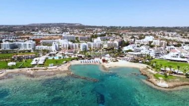 Aerial bird's eye footage view of Pernera beach in Protaras, Paralimni, Famagusta, Cyprus. The famous tourist attraction golden sandy bay with sunbeds, sun umbrellas people swimming in sea from above. Side 360 view.