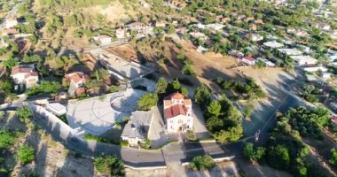 Souni Zanakia, Limasol, Cyprus 'taki Archangel Michael Kilisesi' nin insansız hava aracı görüntüleri. Çan kulesi ve meydanı, Souni Zanatzia ormanı ve seramik çatı mimarisini gün batımında yukarıdan göster.