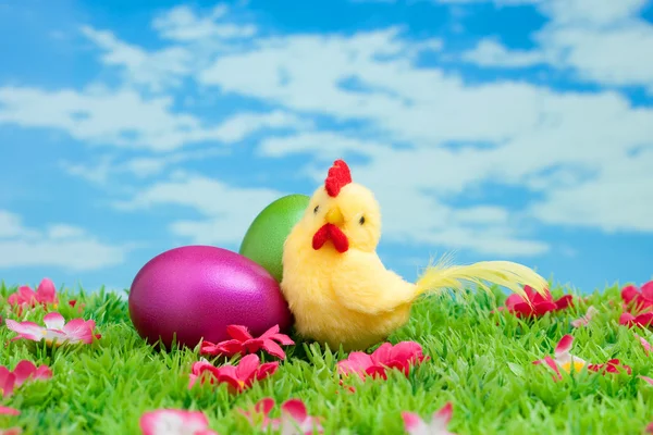 Påskharen gjorda av choklad med påsk ägg på en grön äng med blommor framför en blå himmel — Stockfoto