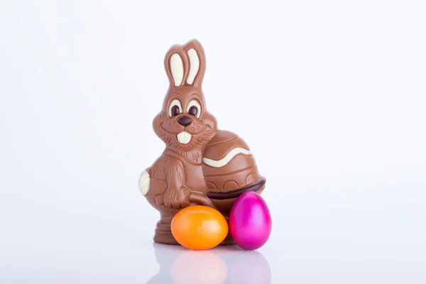 Conejo de Pascua hecho de chocolate con huevo de Pascua en un prado verde con flores frente a un cielo azul —  Fotos de Stock